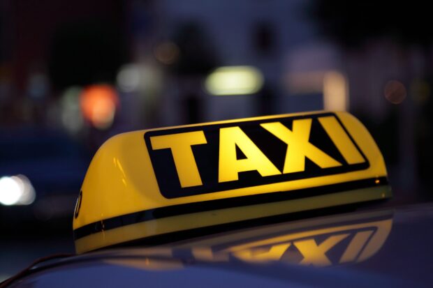 Illuminated taxi sign on top of car at night with a taxi in the city