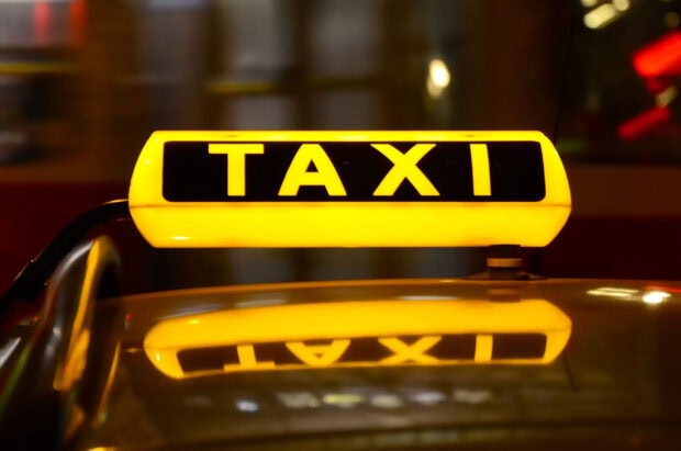 Illuminated taxi sign glowing brightly at night with reflection on car roof