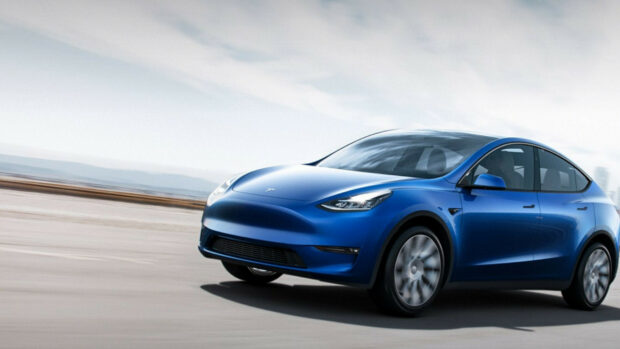 Blue Tesla Model Y driving fast on an open road under a cloudy sky