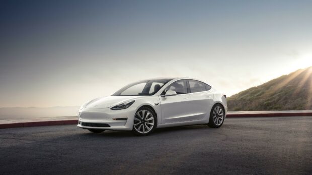 A white Tesla Model Y parked on a road at sunset with mountains in the background