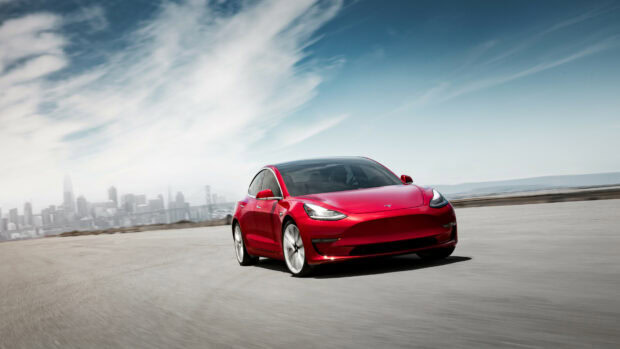 Red Tesla Model Y driving on an open road with city skyline in the background