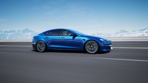 A blue Tesla Model Y driving fast on a mountain road with snowy peaks in the background