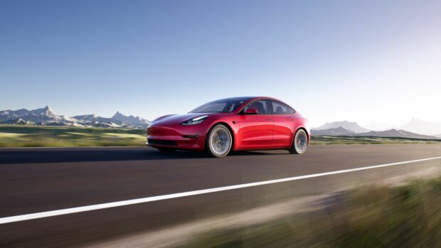 A red Tesla Model Y driving fast on a highway with mountains in the background