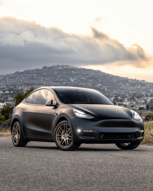 Matte black Tesla Model Y parked on the road with hills in the background