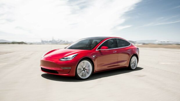 A red Tesla Model Y driving on an open road in a clear sunny day