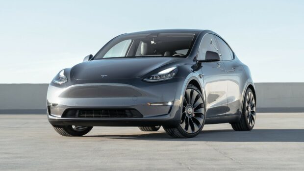 A sleek Tesla Model Y parked on a concrete surface under clear sky with reflective gray body