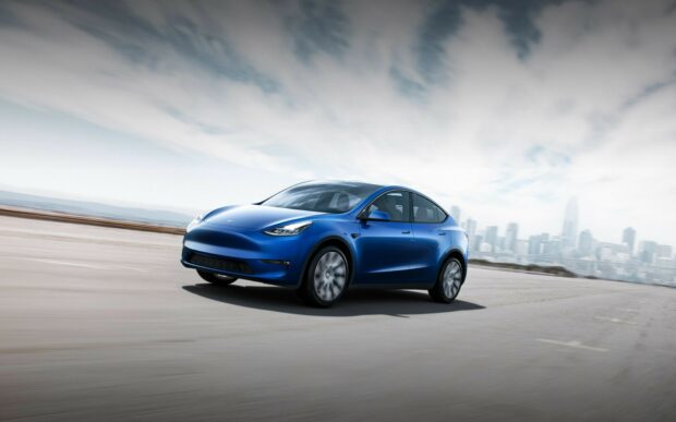Blue Tesla Model Y driving fast on an empty road with city skyline in the background