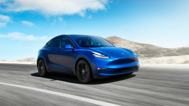Blue Tesla Model Y driving on desert highway under clear sky