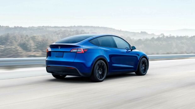 Blue Tesla Model Y driving on the highway with forest in the background
