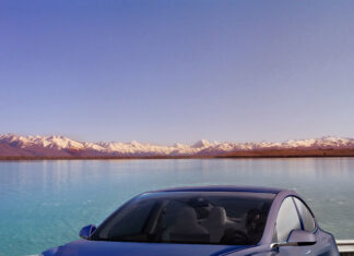 Blue Tesla Model Y driving on road near lake and mountains background