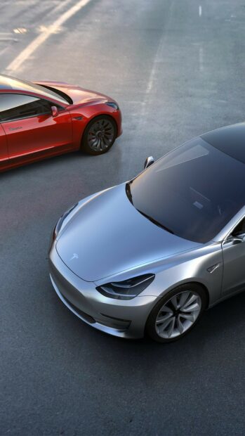 A silver Tesla Model Y parked next to a red Tesla Model Y on a paved surface