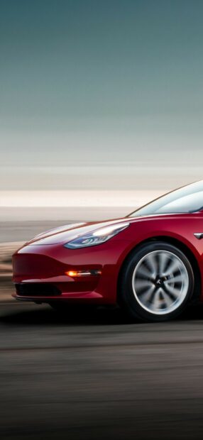 Red Tesla Model Y driving fast on a blurred road with clear sky in the background