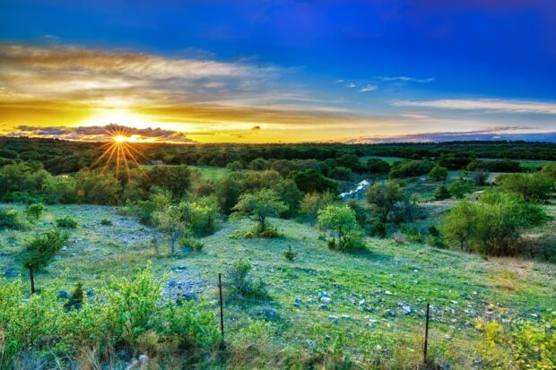 A scenic view of Texas Hill Country with lush greenery and a sunset in the sky