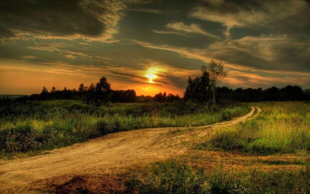A winding dirt road through green fields under a dramatic sunset sky in Texas Hill Country