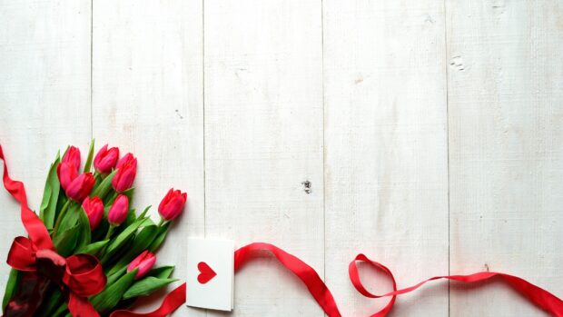 A bouquet of red tulips with a heart card and red ribbon on a wooden surface