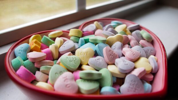 Heart shaped candy with love and kiss messages in a red container on a windowsill