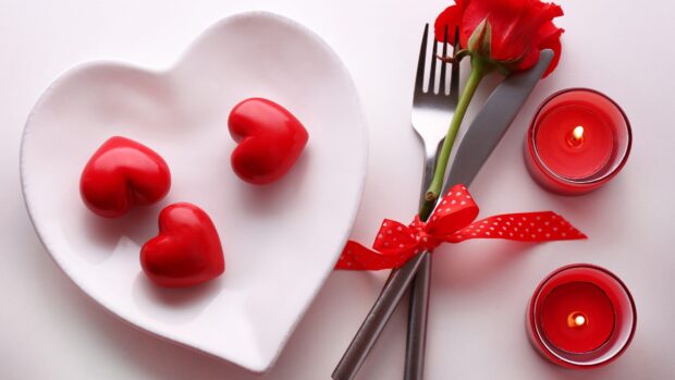 Red hearts on a plate with a rose and candles symbolizing valentine celebration