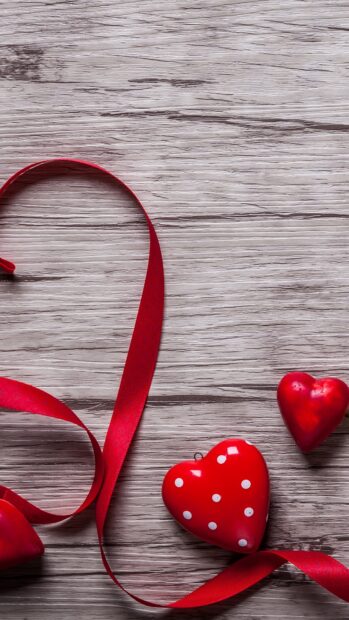 Red ribbon forming a heart shape with heart decorations on wooden surface for love celebration