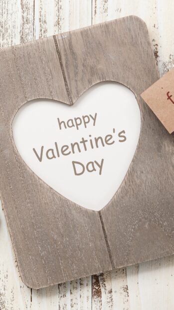 Heart shaped wooden frame with happy Valentine's Day message on white paper