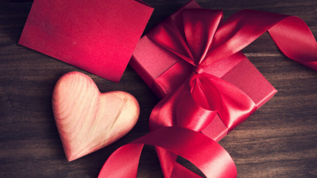 A wooden heart and a Valentine gift box with a red ribbon on a wooden table