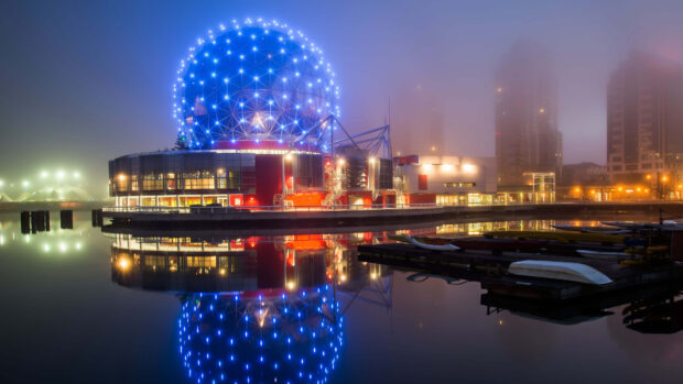 The iconic Vancouver Canada geodesic dome with bright blue lights reflecting on calm water at night