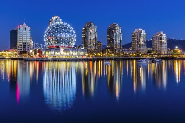 The illuminated science center sphere in Vancouver Canada reflecting over calm water at night