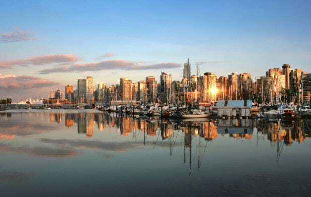 Vancouver city skyline reflects on calm water with boats in the harbor at sunset