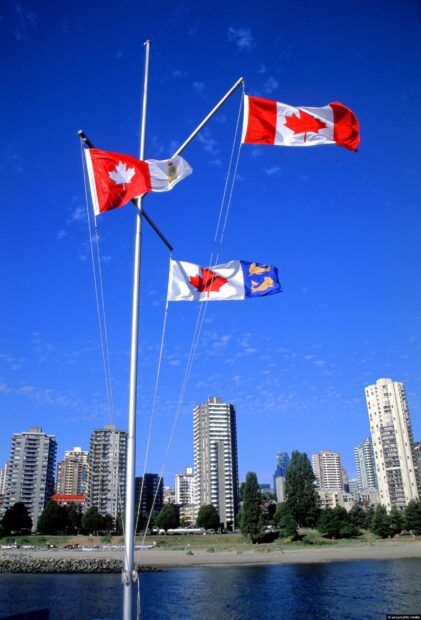 Canadian flags flying over Vancouver Canada skyline on a clear blue sky day
