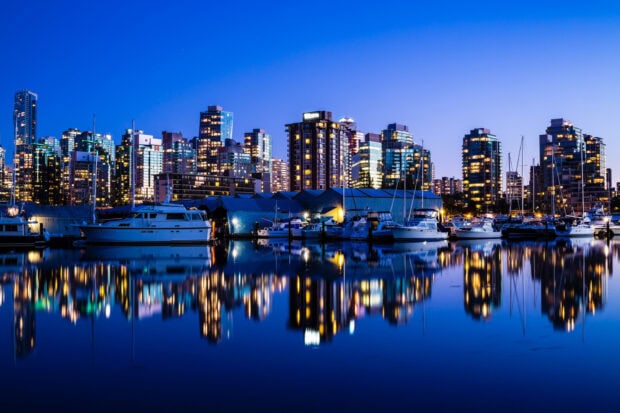 Evening view of Vancouver Canada skyline with boats reflecting on calm water