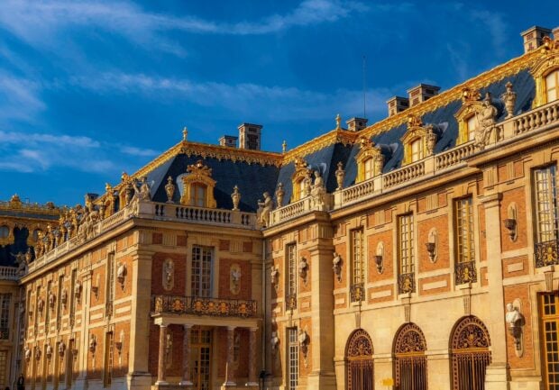 The ornate facade of Versailles palace with classical statues and golden details under a clear blue sky