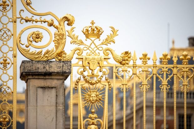 Ornate gold Versailles gate with sun emblem and crown decoration