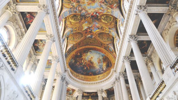 The ceiling artwork and grand columns inside Versailles palace showcasing Versailles architecture
