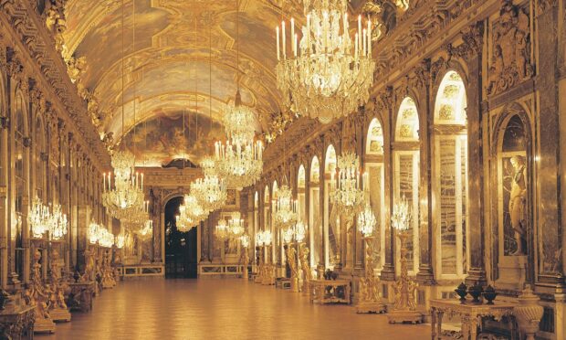 The grand corridor inside Versailles with ornate golden decorations and luxurious chandeliers lighting the hallway