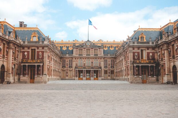 The grand facade of Versailles palace with French flag under a blue sky