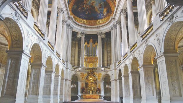 The grand interior of a Versailles cathedral with ornate columns and a decorated ceiling mural