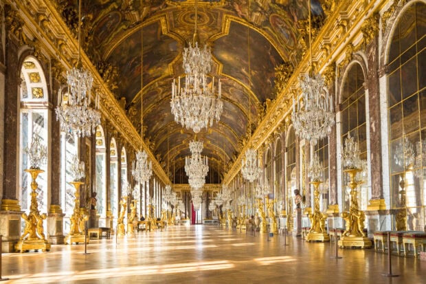 The grand Versailles gallery decorated with golden statues and crystal chandeliers