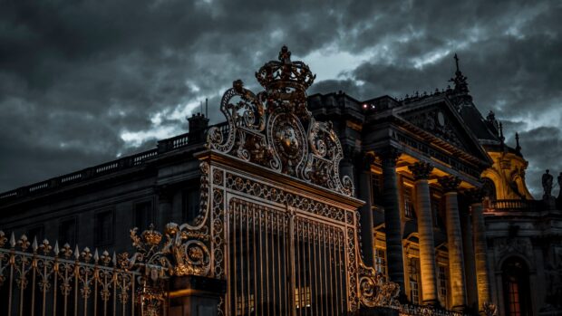Ornate Versailles gate and palace illuminated at dusk under dark dramatic clouds
