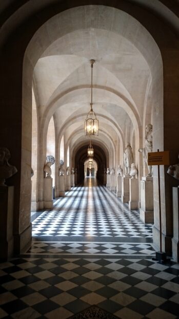 A long corridor in Versailles decorated with marble busts and hanging lanterns under stone arches