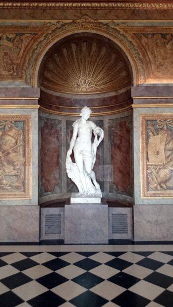 Marble statue inside Versailles palace with detailed marble walls and checkered floor