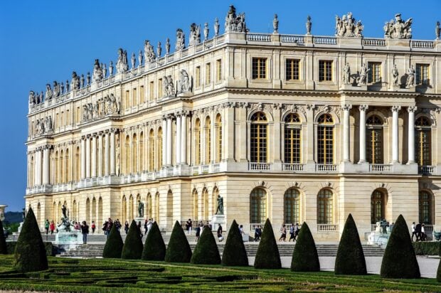The detailed architecture of Versailles with sculptures and windows under a clear blue sky