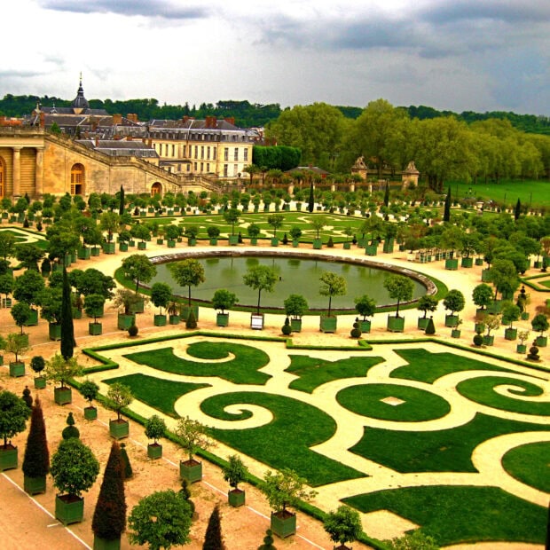 The Versailles garden showcases elegant geometric patterns and lush greenery under a cloudy sky