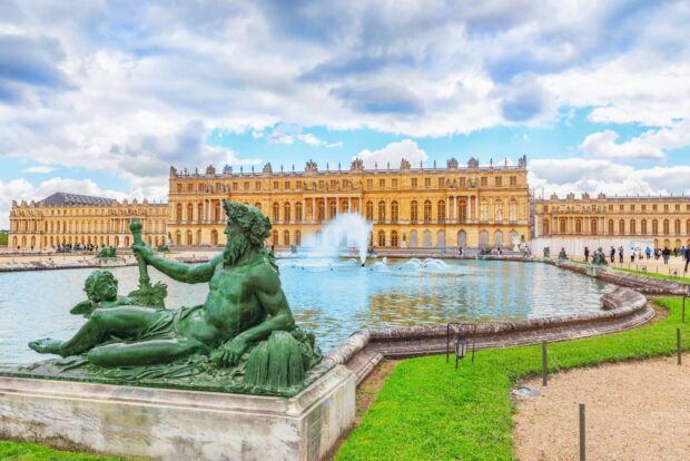 The Versailles statue and palace in the garden with fountains under a cloudy blue sky