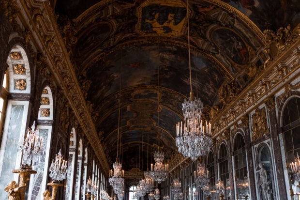 The grand interior of Versailles with ornate chandeliers and detailed ceiling paintings in HD quality