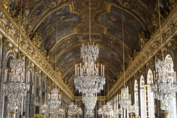 Ornate Versailles ceiling with chandeliers and detailed gold decorations inside the palace