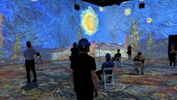People viewing a Vincent Van Gogh art exhibition featuring Starry Night indoors