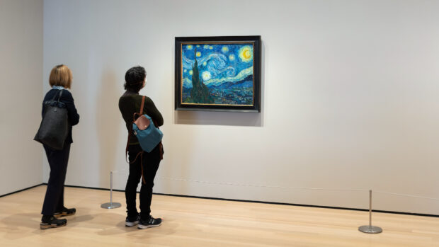Two people watching a Vincent Van Gogh painting in an art gallery