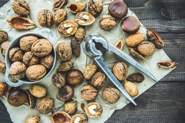 A rustic arrangement of walnuts in shells with a metal nutcracker on parchment paper