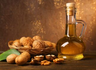 A basket of walnuts with a glass bottle of walnut oil on a wooden surface and a green leaf nearby