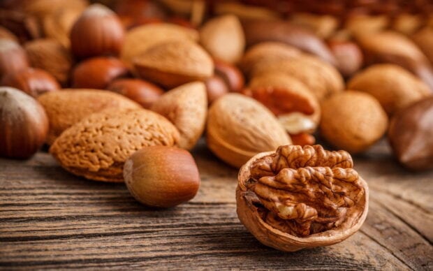 Close up of walnuts and assorted nuts on a wooden surface with a walnut kernel in focus
