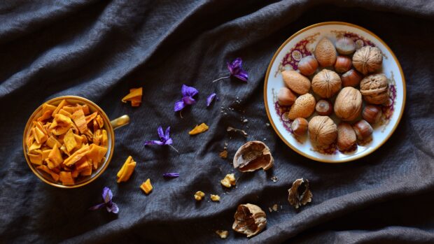 A plate of assorted nuts including walnuts and hazelnuts on a patterned plate on dark fabric